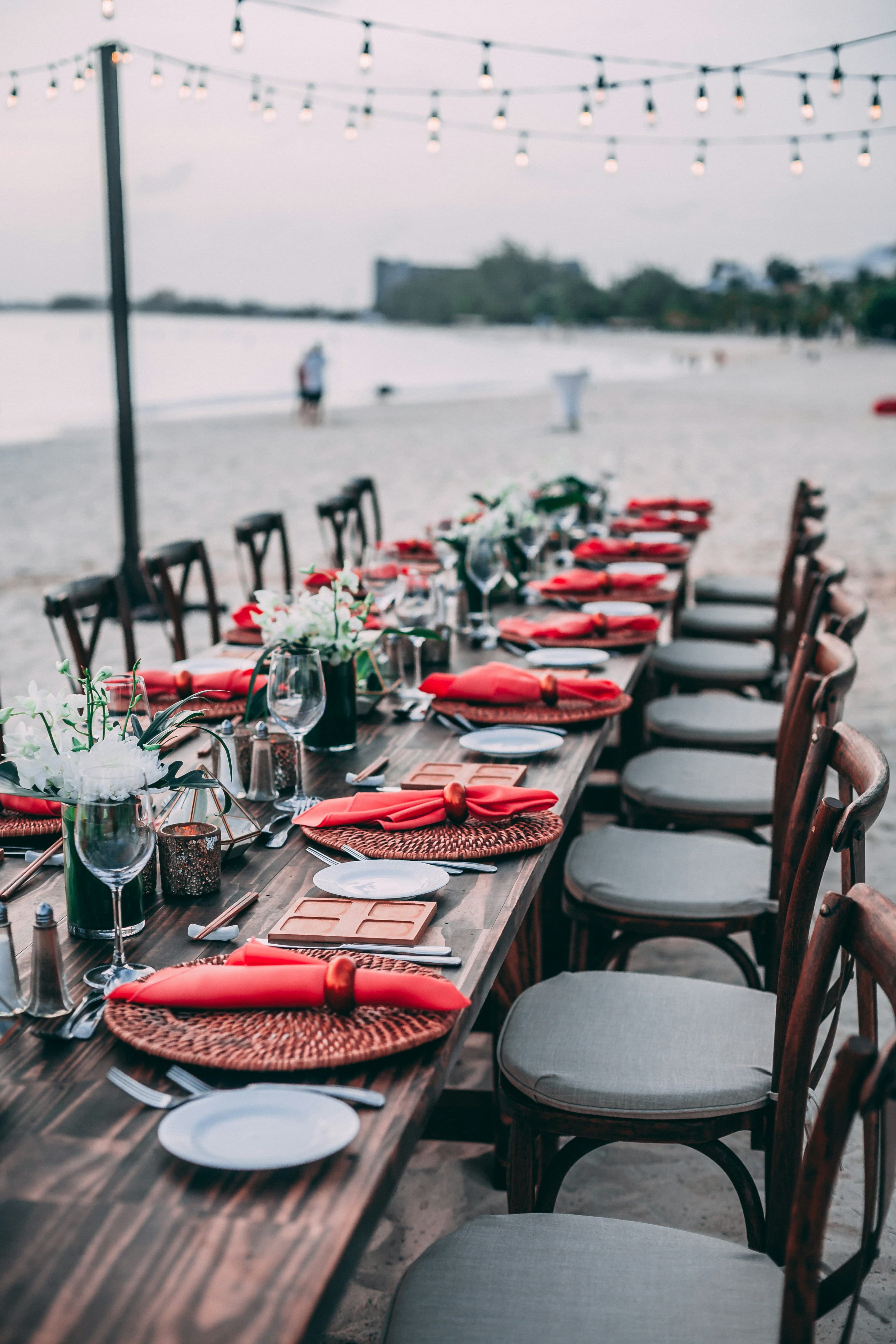 Outdoor event table set beside the water with red napkins and white flowers